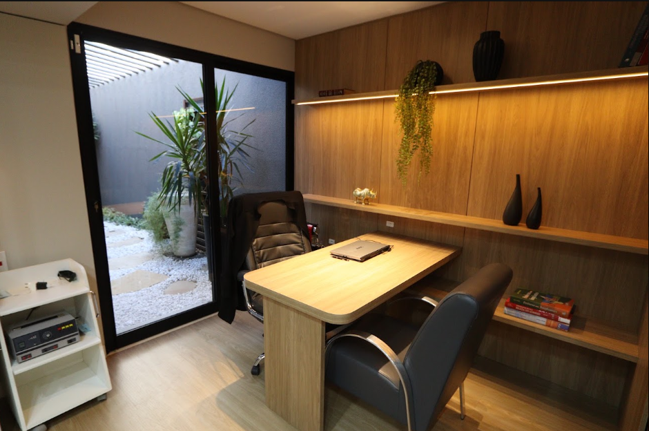 Recepção da clínica odontológica Perfecta Odontologia, ambiente moderno com marcenaria em madeira clara, iluminação embutida aconchegante, plantas decorativas, poltronas de couro e janela com vista para jardim interno, fotografia realista